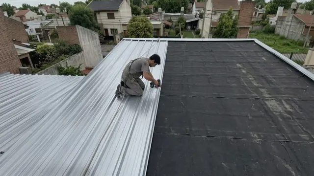 Techista con arnés atornillando chapas acanaladas nuevas sobre el techo de una casa